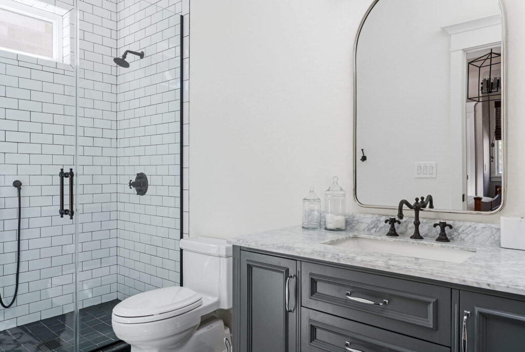 A modern bathroom with a glass-enclosed shower, white subway tile, and a gray vanity with a marble countertop ensures clear drains and smooth flow in all drain lines—perfect for holiday plumbing peace of mind. Two glass jars sit on the counter.