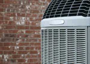 An air conditioning unit is operating outdoors in front of a red brick wall. The fan on top of the unit is rotating, indicating that the system is running.