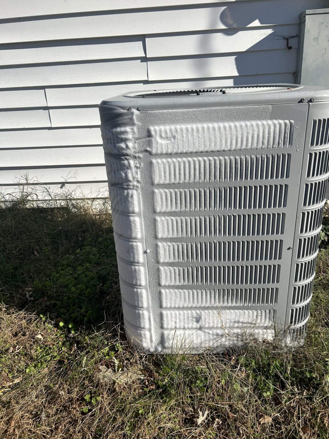 A central air conditioning unit outside a house is covered with a thick layer of frost or ice, highlighting the need for AC repair San Diego services as sunlight casts shadows on the nearby white siding and grass.