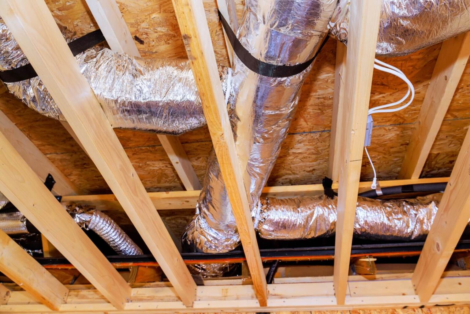 Exposed wood ceiling beams with HVAC ductwork wrapped in reflective insulation and visible air duct sealing. Some electrical wiring is attached to the beams, highlighting attention to both HVAC sealing and system organization.