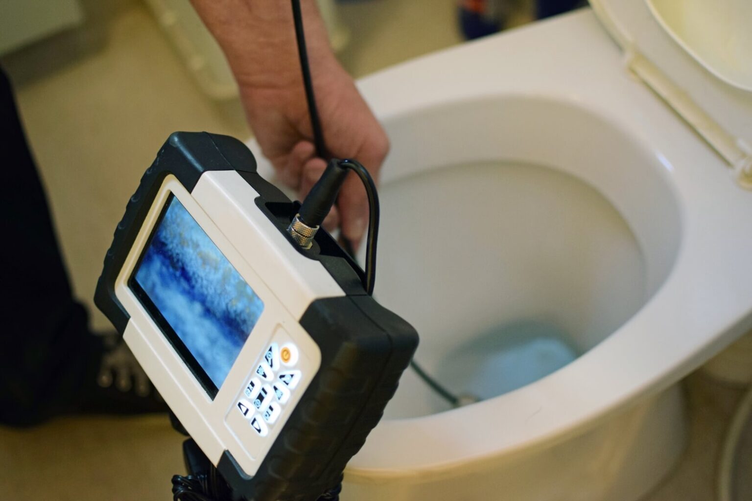 A person holds a sewer inspection camera near the opening of a toilet, with the camera monitor displaying an image from inside the drain—a typical scene during a Camera Inspection Service San Diego residents rely on for plumbing issues.