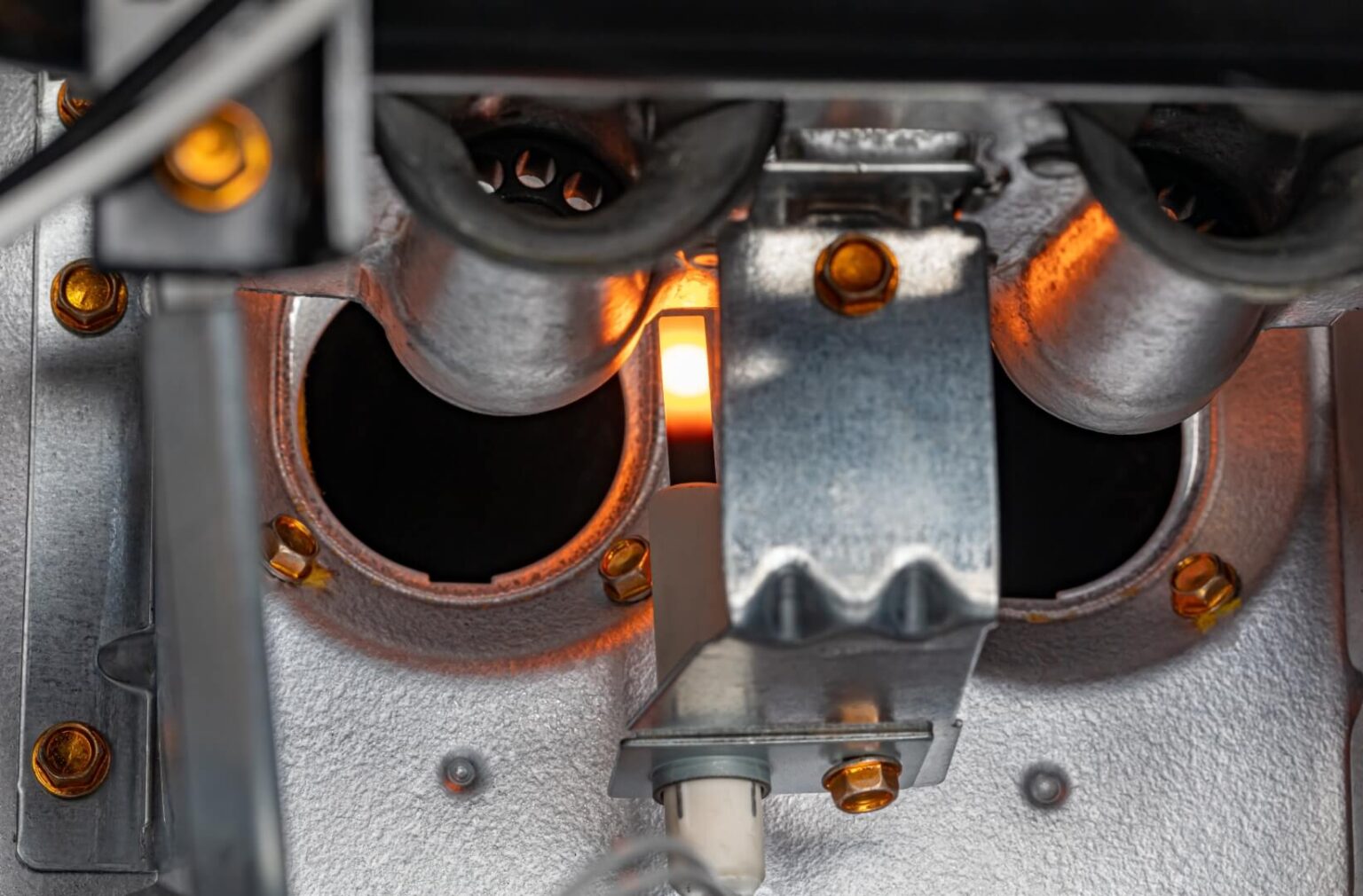Close-up view of the interior of a gas furnace, showing the burners ignited with a visible orange flame, metal components, and screws—a detailed look often seen during furnace repair.