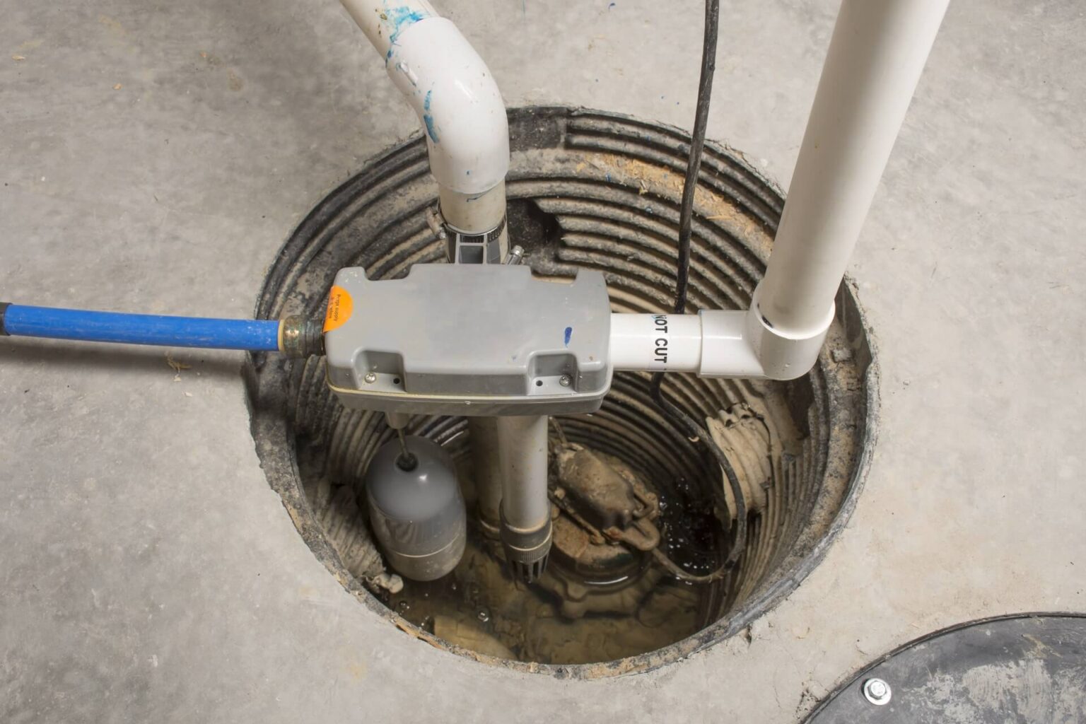 A close-up view of a sump pump system installed in a concrete basement floor highlights pipes, wiring, and the pump mechanism inside a circular sump pit—demonstrating professional Sump Pump Install San Diego expertise.