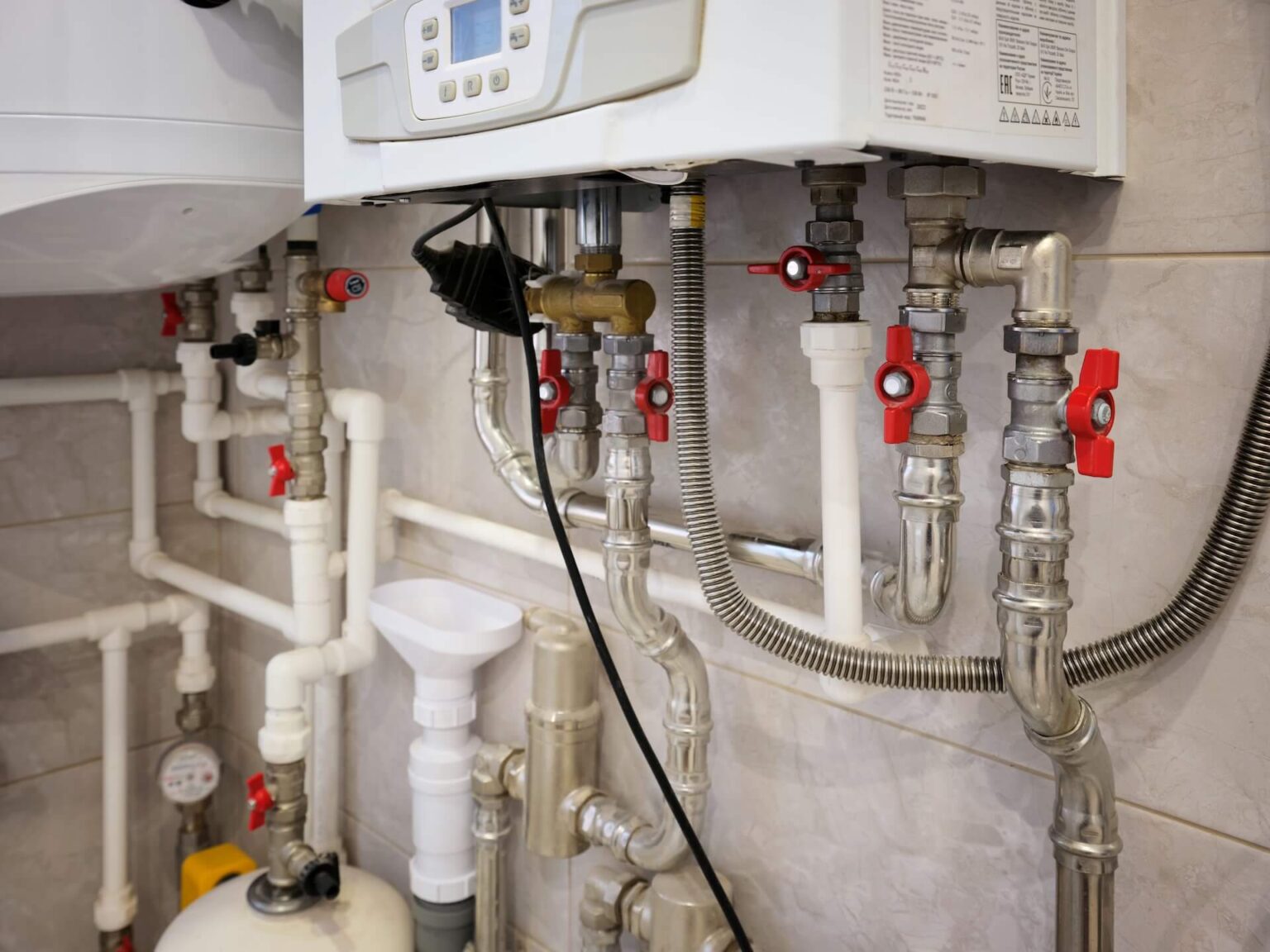 A close-up view of a heating system’s plumbing, highlighting pipes, valves with red handles, a pressure gauge, and control panels—ideal for those seeking Tankless Water Heater Repair insights.