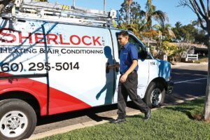 A man in a blue shirt walks toward a white van with "Sherlock Heating & Air Conditioning" and a phone number printed on the side. The van is parked on a residential street on a sunny day.